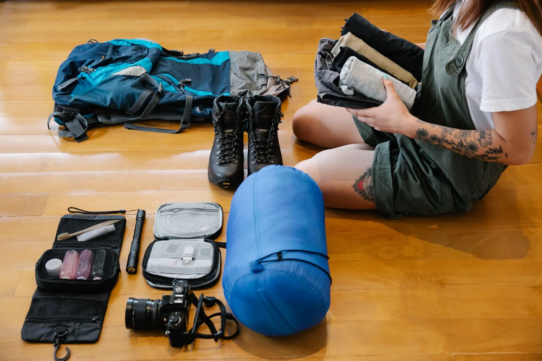 Ausruestung auf dem Boden ausgelegt: Rucksack, Schuhe, Kleinteile und ein im Packsack verstauter Schlafsack