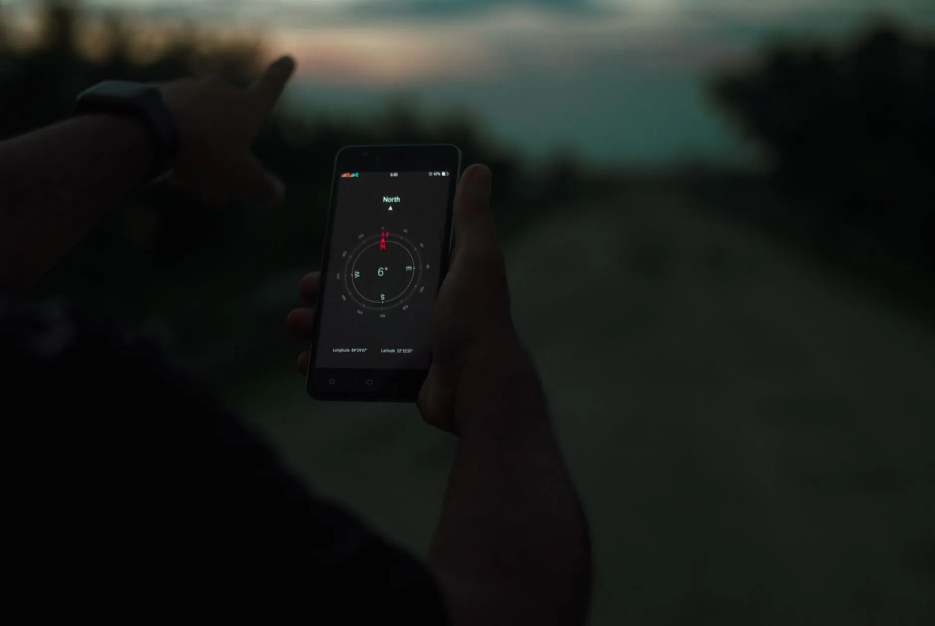 Hand haelt ein Smartphone mit geoeffneter Kompass-Anzeige, dahinter daemmriger Himmel
