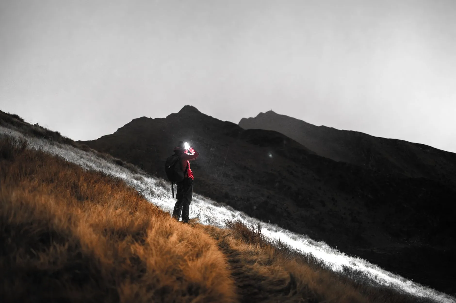 Einzelne Person mit eingeschalteter Stirnlampe auf einem Bergpfad in der Daemmerung