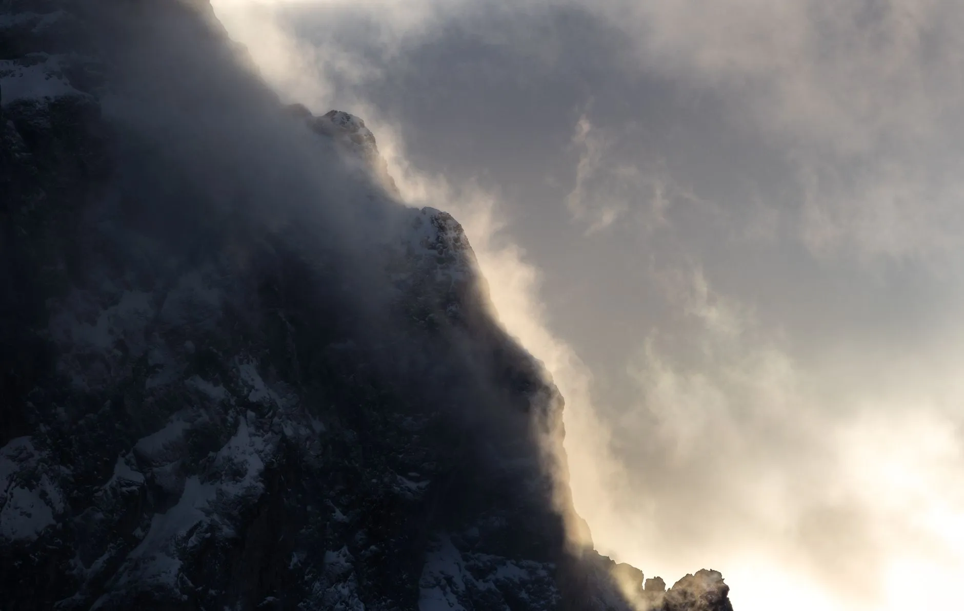 Wolken und Schneefahnen ziehen im Gegenlicht ueber einen schneebedeckten Felsgrat